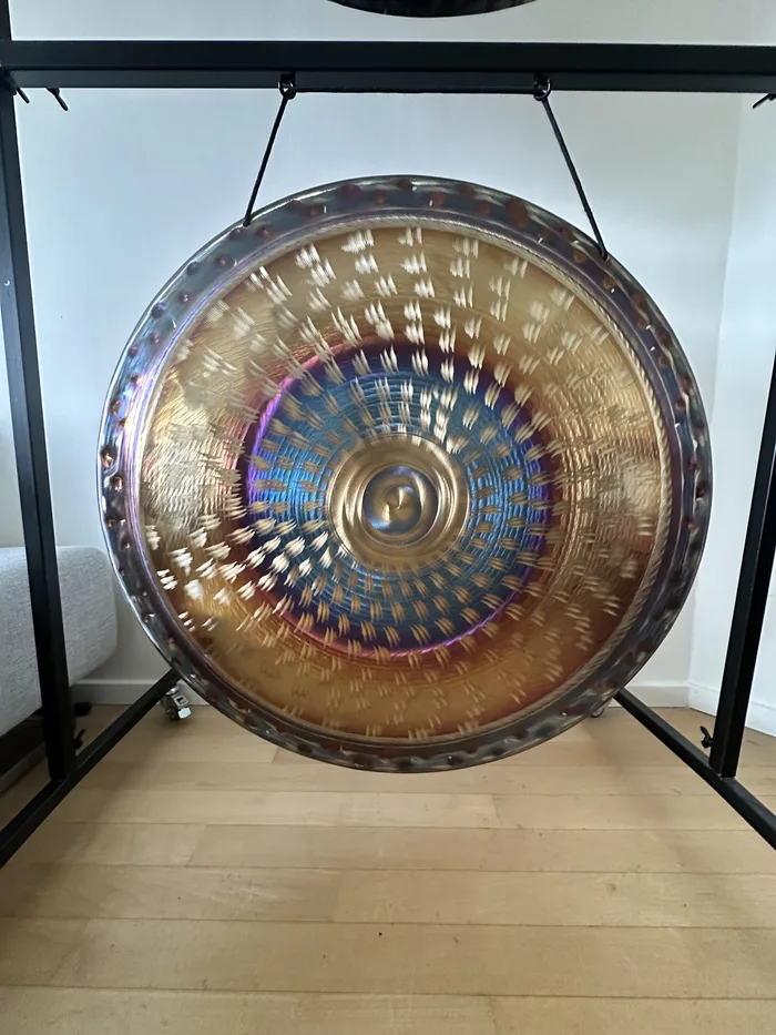 Close-up of a flame-treated gong, its surface rippling with bronze, violet and blue patina